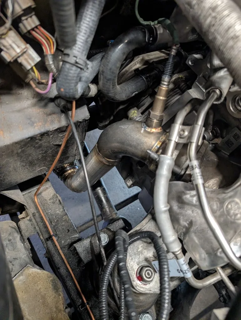Downpipe met O2-sensorbung in de motorruimte van de Defender